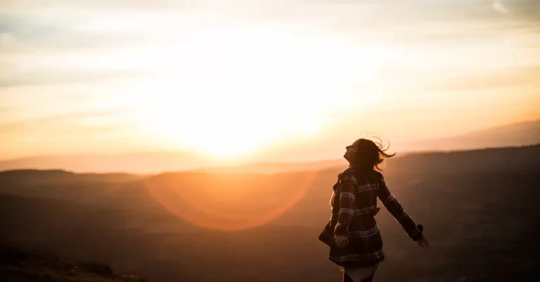 Mulher refletindo ao pôr do sol, em um momento de paz e introspecção, simbolizando perguntas de autoconhecimento.